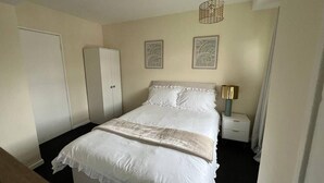 A neatly arranged bedroom with a bed, a wardrobe, and a nightstand with a lamp. - Walthamstow - Apartment - Stay 3 - Street Parking (London)