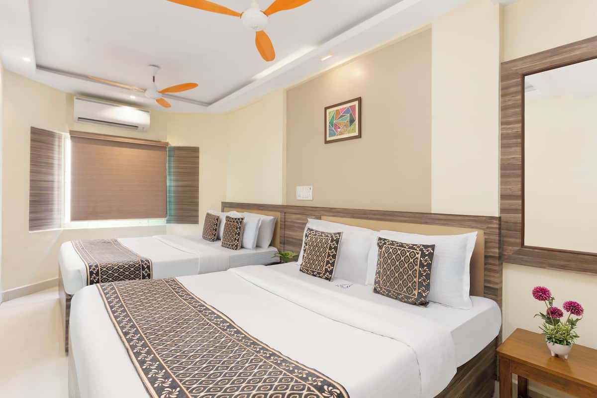 A hotel room with two beds, a ceiling fan, an air conditioning unit, a framed picture, and a small table with flowers.
