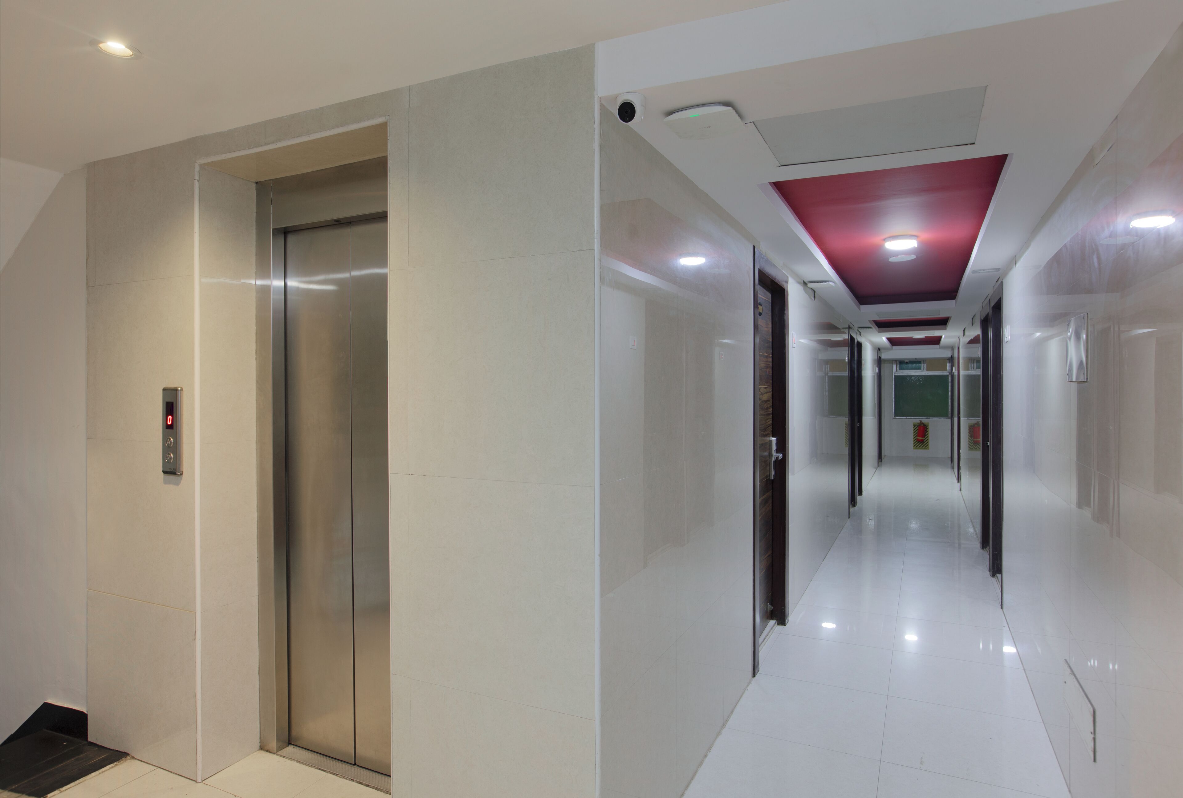 Corredor moderno com elevador, teto vermelho e chão revestido de azulejos.