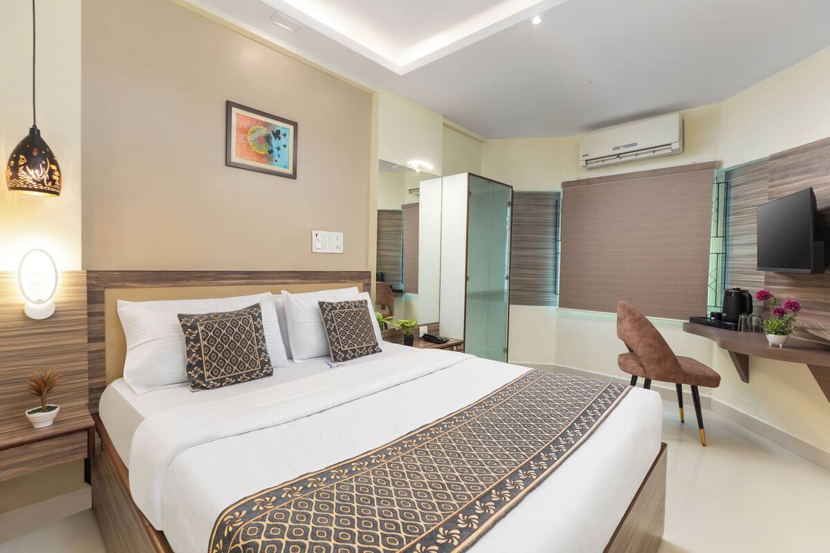 A modern hotel room with a large bed, bedside table, and a desk with a chair.