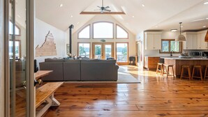 Een ruime woonkamer met een grote houten bank, een grijze bank en een plafondventilator van hout.