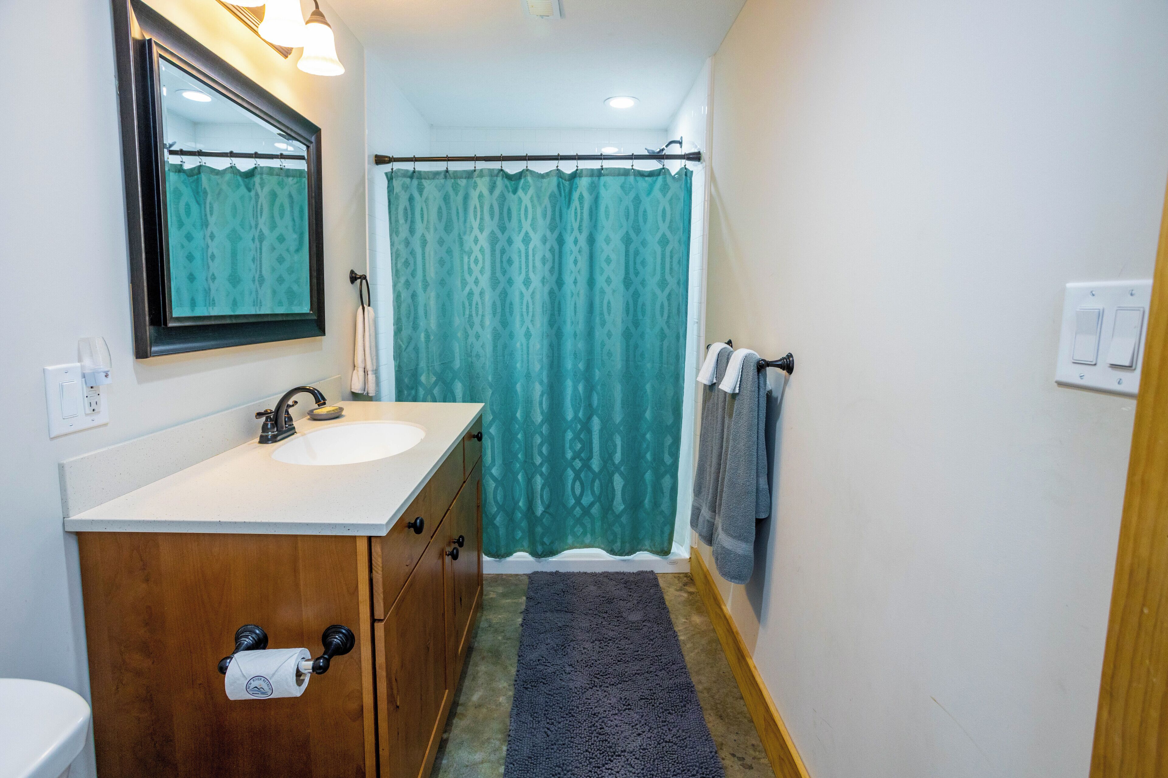 A bathroom with a wooden vanity, a sink, a mirror, a shower curtain, and a towel rack.