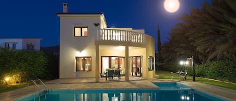 A two-story building with a pool in front, featuring a balcony with outdoor seating and a view of the moon.