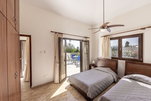 Une chambre avec deux lits, un ventilateur de plafond, une fenêtre avec des rideaux et une vue sur l’extérieur.