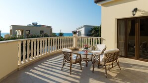 A balcony with a table and chairs, a view of the sea, and a building with a tiled roof. - Villa Tsikkos Pende in Argaka (Argaka)