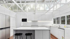 A modern kitchen with white cabinetry, a central island with stools, and a large window providing natural light.