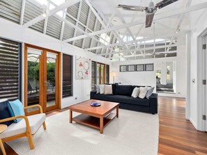 A spacious living area with a large sofa, a coffee table, and a chair. There are sliding glass doors leading to an outdoor area.