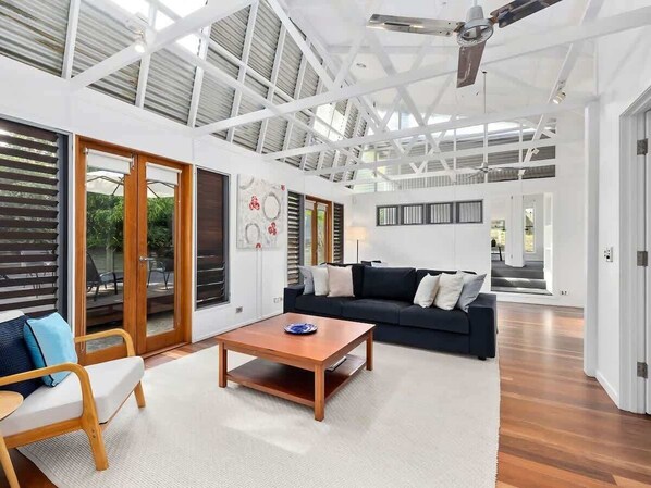 A spacious living area with a large sofa, a coffee table, and a chair. There are sliding glass doors leading to an outdoor area.