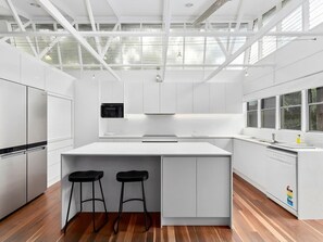 A modern kitchen with white cabinetry, a central island with stools, a built-in microwave, and a window overlooking the outdoors.