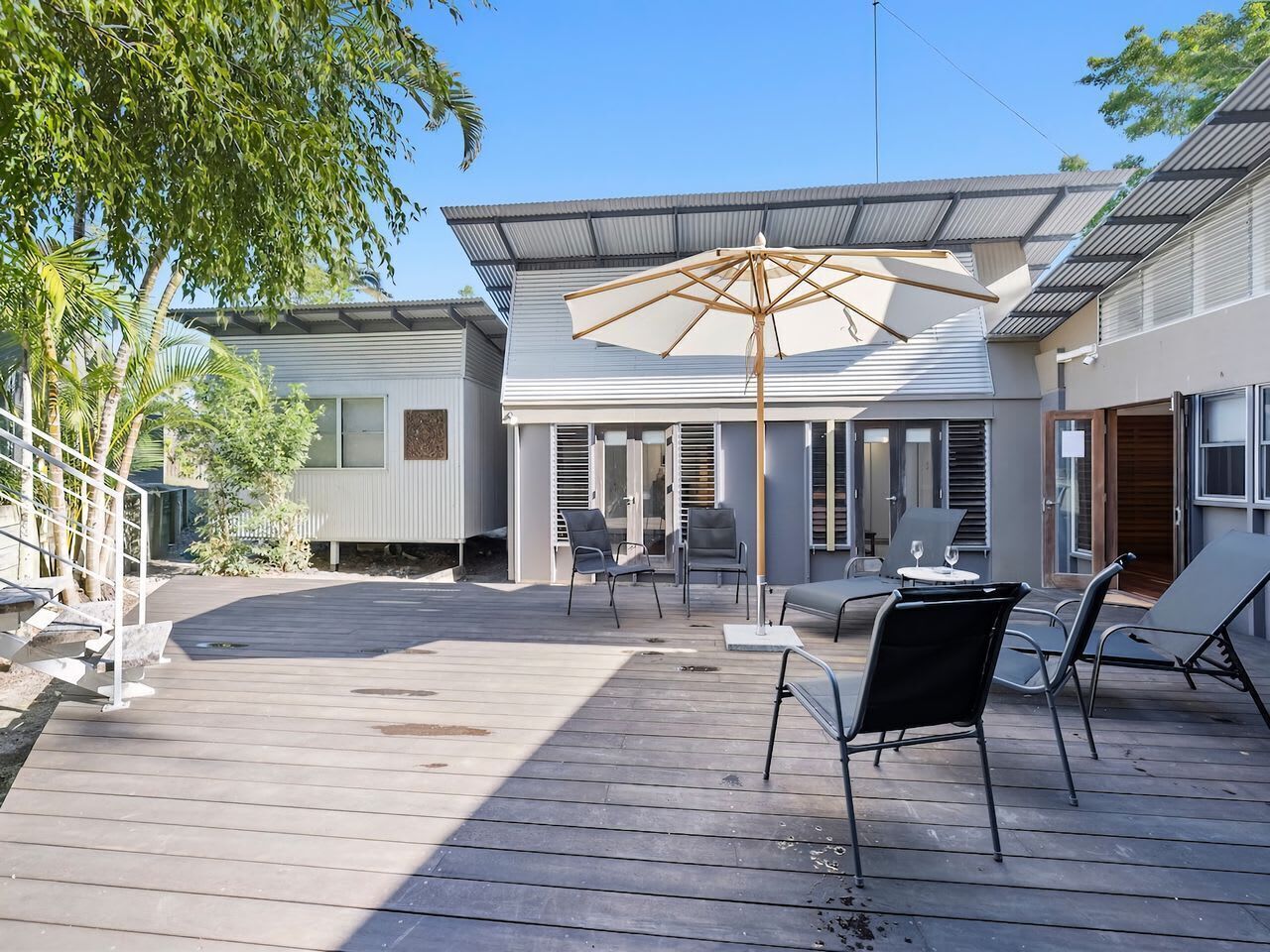 A covered outdoor patio with a wooden deck, outdoor seating, and a large umbrella.
