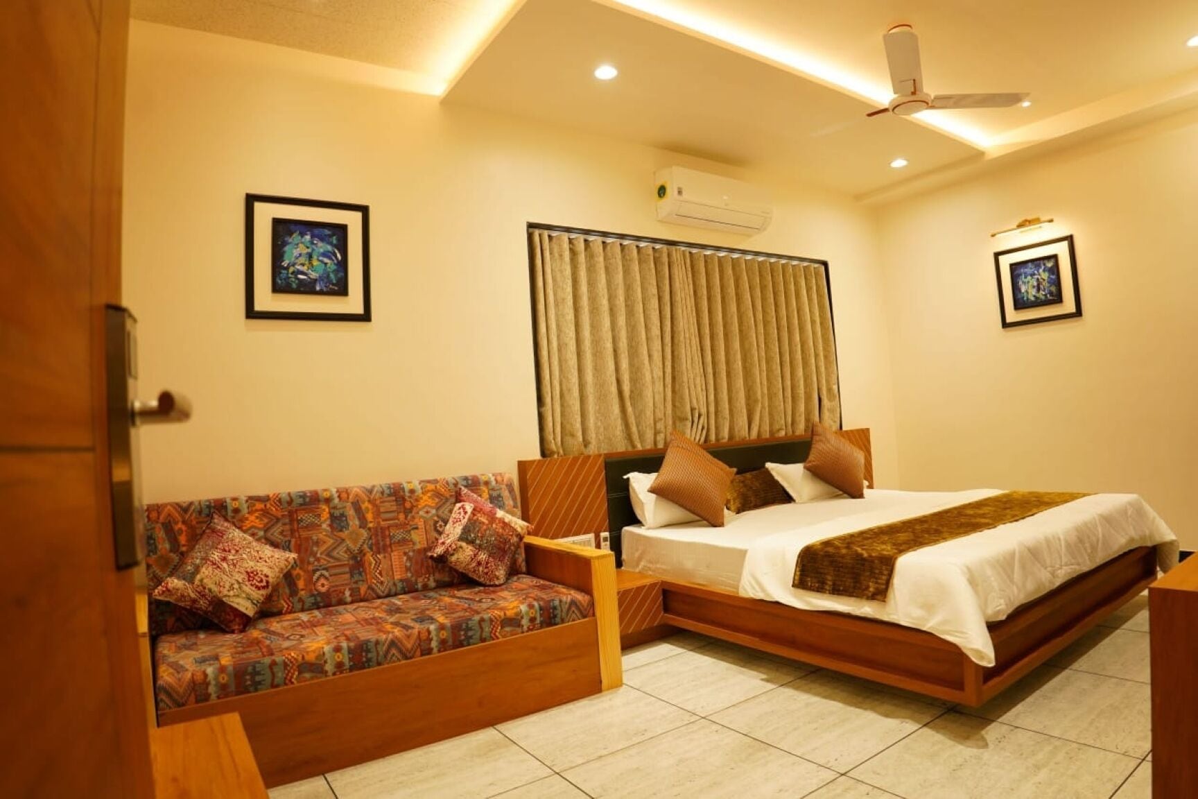 A hotel room with a sofa, a bed, a ceiling fan, and an air conditioning unit.