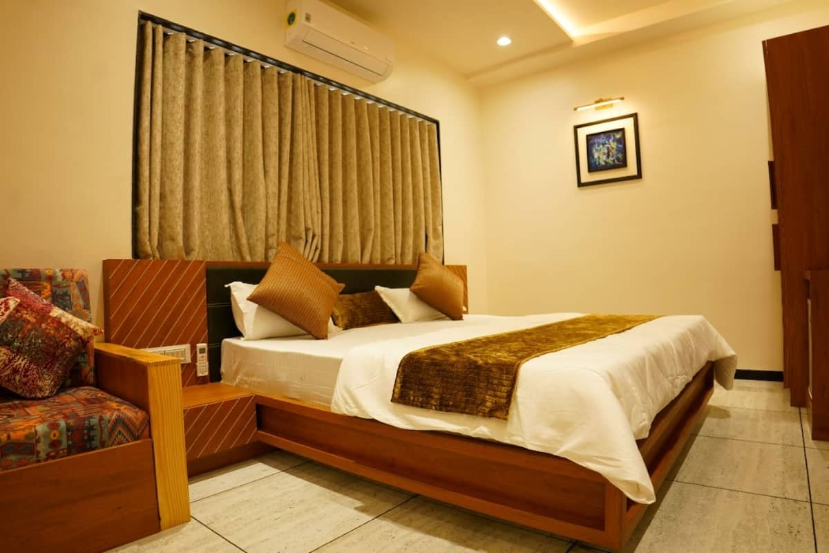 A hotel room with a large bed, a wooden headboard, a chair with a patterned cushion, and a framed picture on the wall.