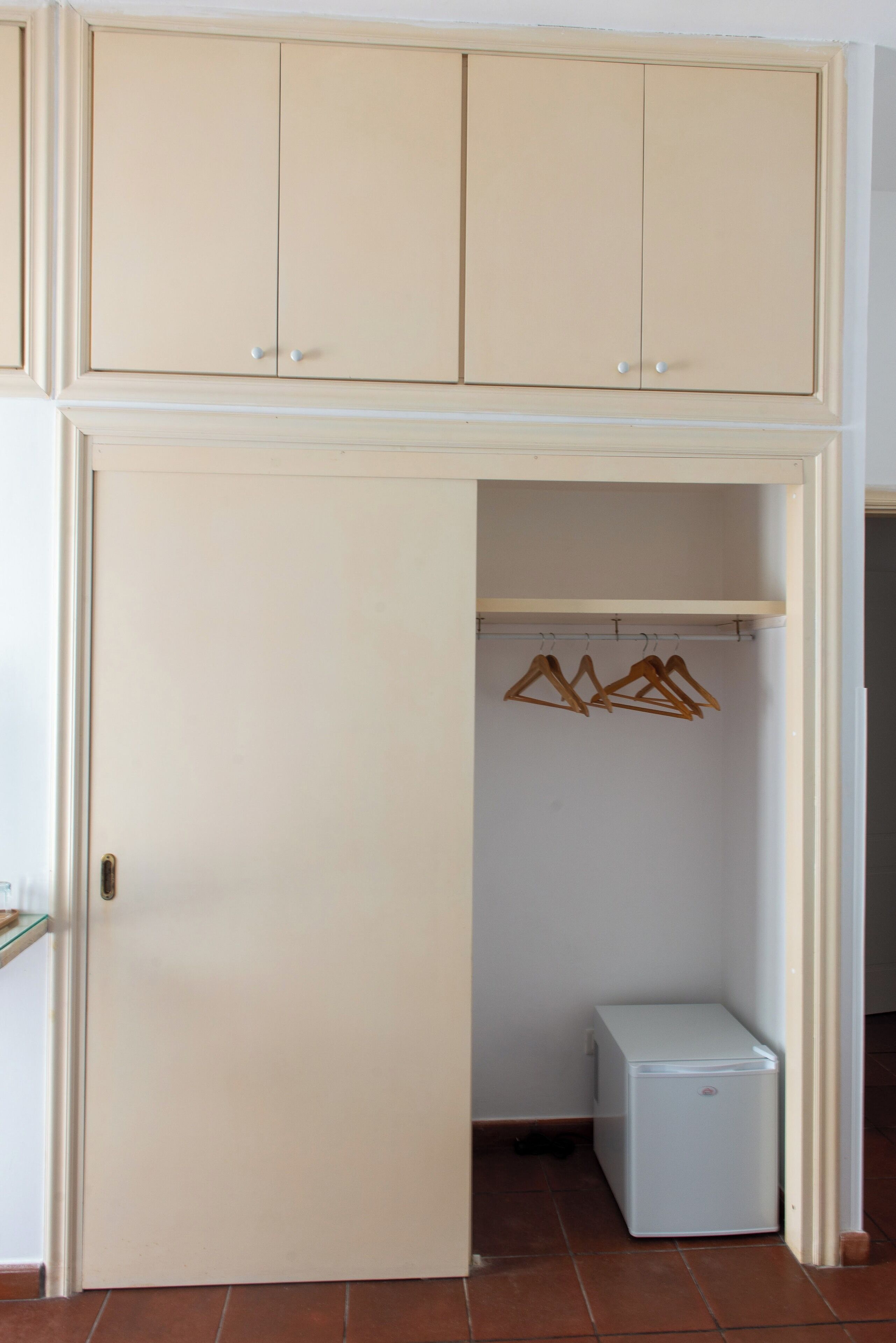 Een kamer met een kledingkast, een kleine koelkast en een kledingrek.