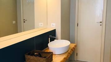 A modern bathroom with a large mirror, a wooden vanity, a white sink, and a small trash can.