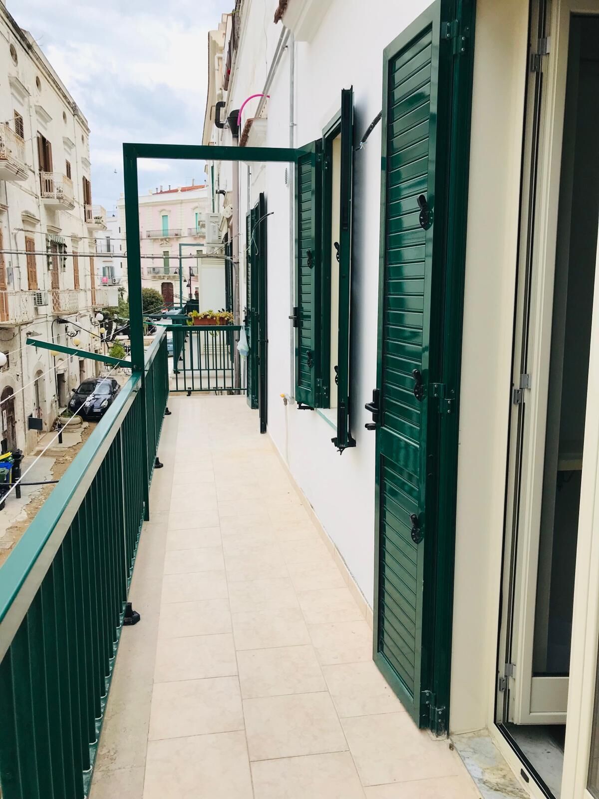 A narrow balcony with green shutters, a tiled floor, and a view of adjacent buildings.