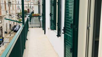 A narrow balcony with green shutters, a tiled floor, and a view of adjacent buildings.