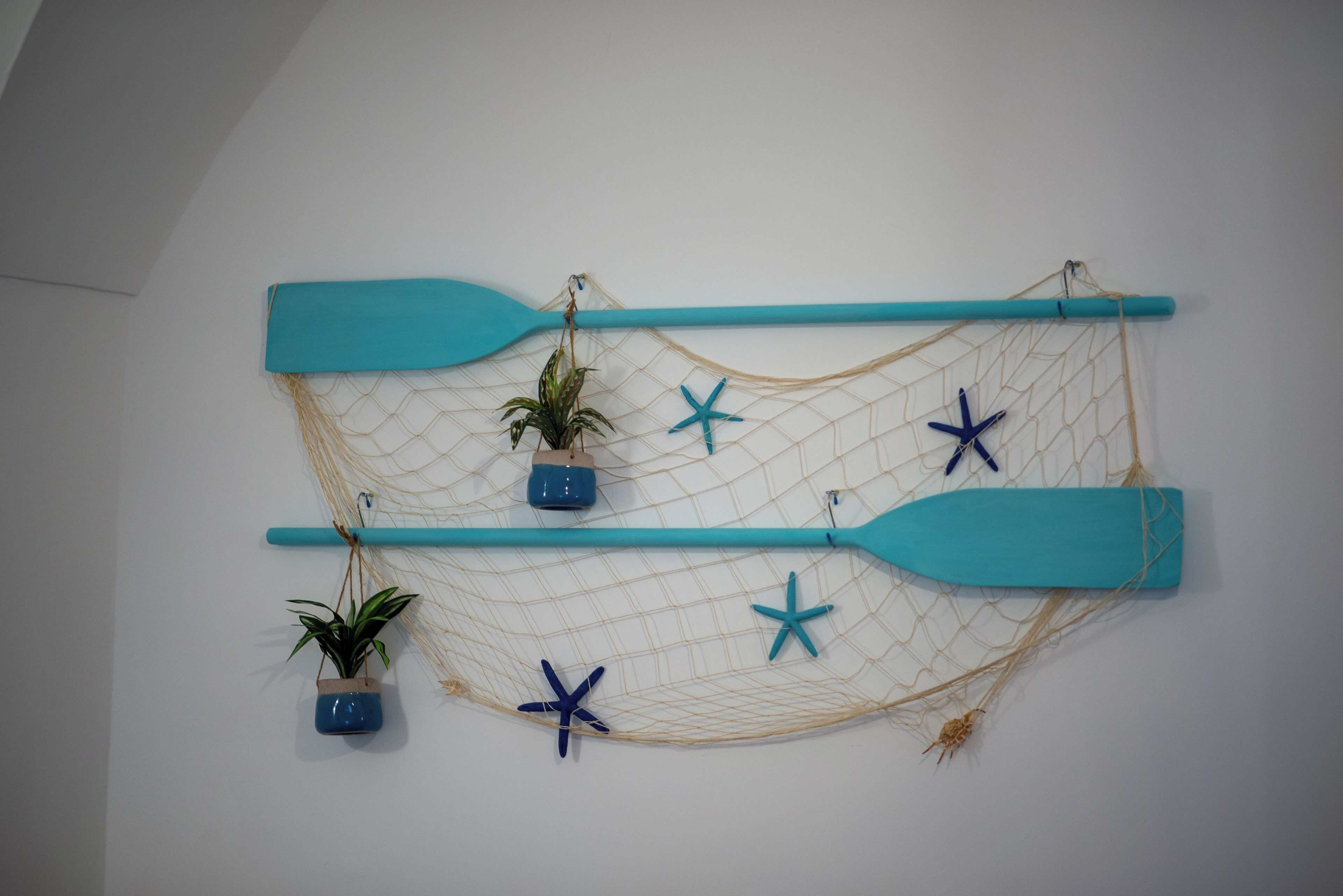 Un élément de décoration murale sur le thème de la mer, comprenant un filet, une étoile de mer et deux pagaies bleues.