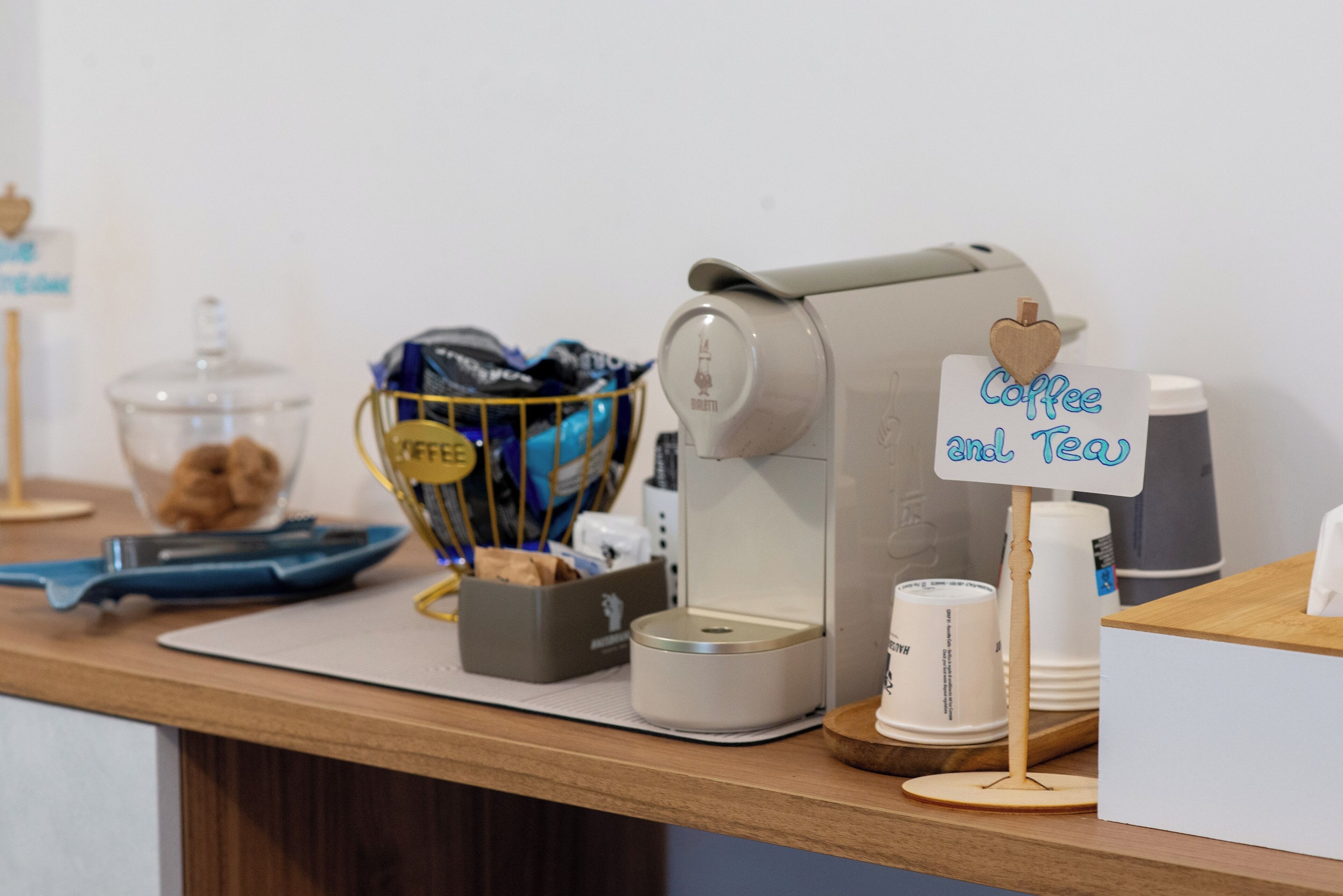 A coffee station with a coffee maker, a sign that says "Coffee and Tea," and a basket of pastries.