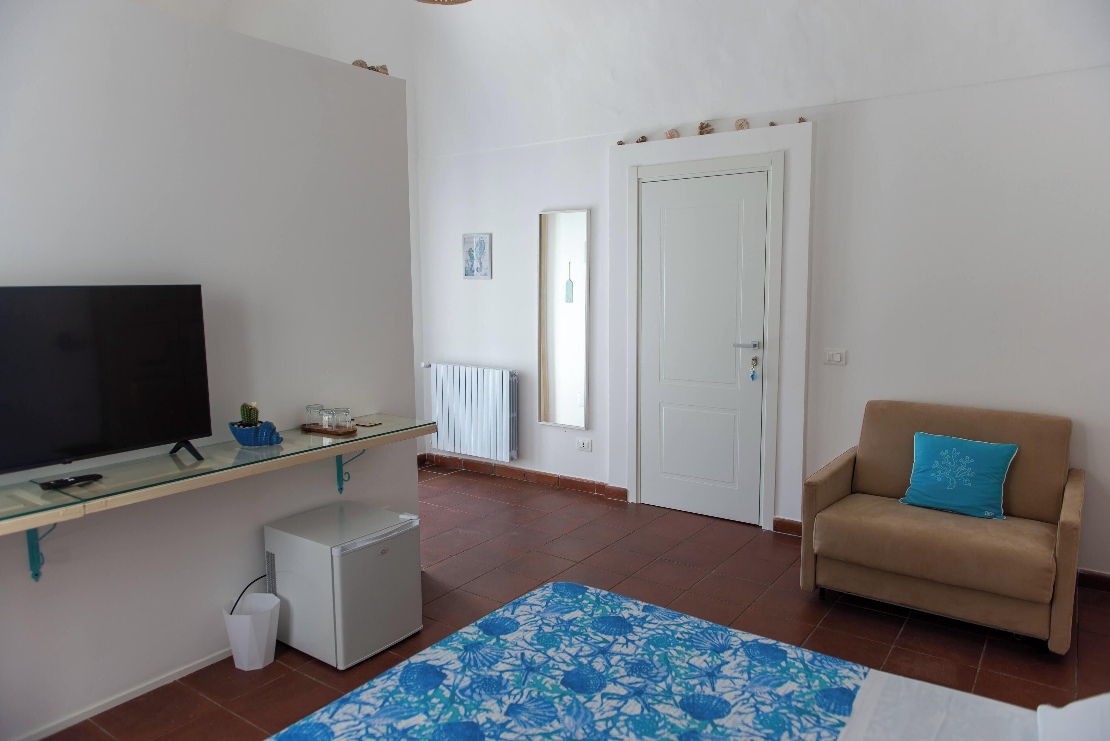 A compact living space with a flat-screen TV, a small refrigerator, a sofa, and a patterned rug.
