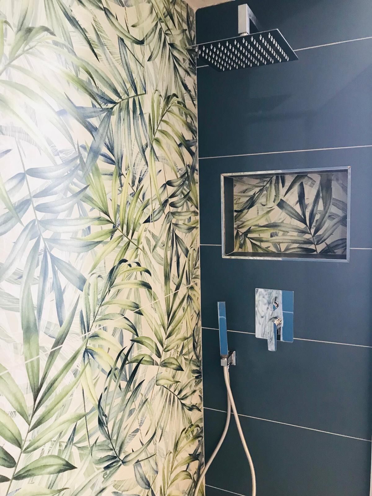A bathroom with a large mirror, a shower with a rain showerhead, and a wall with a tropical leaf pattern.