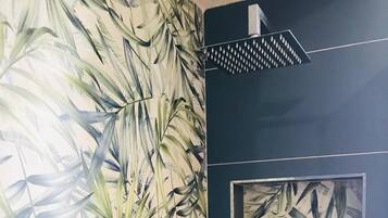 A bathroom with a large mirror, a shower with a rain showerhead, and a wall with a tropical leaf pattern.