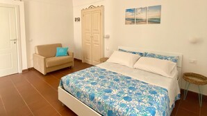 A bedroom with a bed, a sofa, a wardrobe, and a wall-mounted shelf. - Casa Chicchella (Vieste)