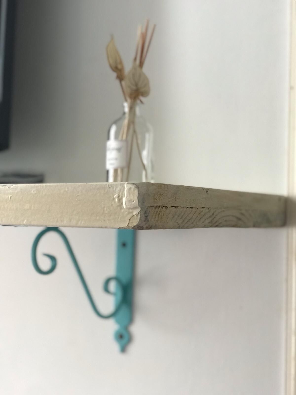 Una repisa con un objeto decorativo y un gancho metálico color turquesa.