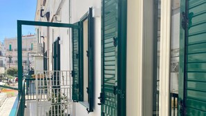 A narrow balcony with green shutters, a white tiled floor, and a view of adjacent buildings. - Casa Chicchella (Vieste)