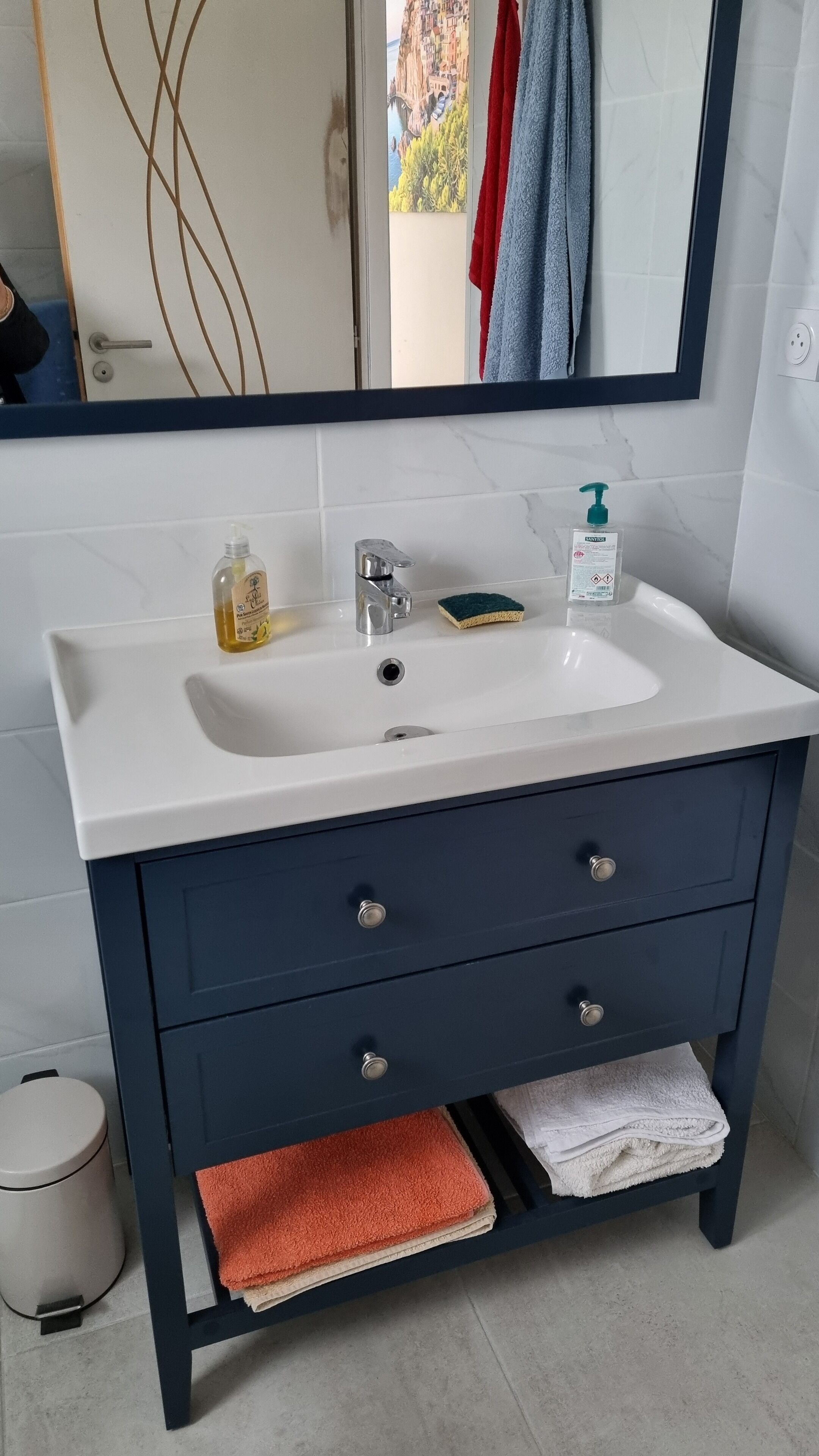 Une salle de bain avec un lavabo blanc, un meuble bleu foncé et un miroir au-dessus.