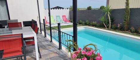 Un patio cubierto con piscina, mobiliario exterior y macetas con flores.