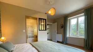 A bedroom with a bed, a hanging light fixture, a window with curtains, and a radiator.