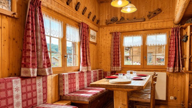 Ein Holzblockbau-Innenraum mit einem Esstisch, Bänken und Blick ins Freie.