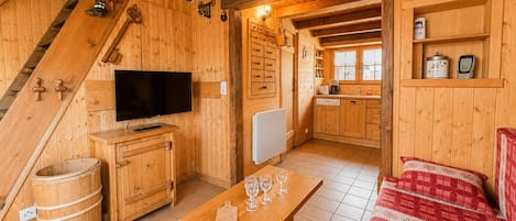 Un interior de madera con una televisión, muebles de madera, una mesa de comedor con vasos, un sofá rojo a cuadros y una zona de cocina.