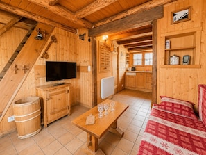 A wooden interior with a TV, wooden furniture, a dining table with glasses, a red checkered sofa, and a kitchen area. - Cozy chalet in village center, near slopes (Notre-Dame-de-Bellecombe)