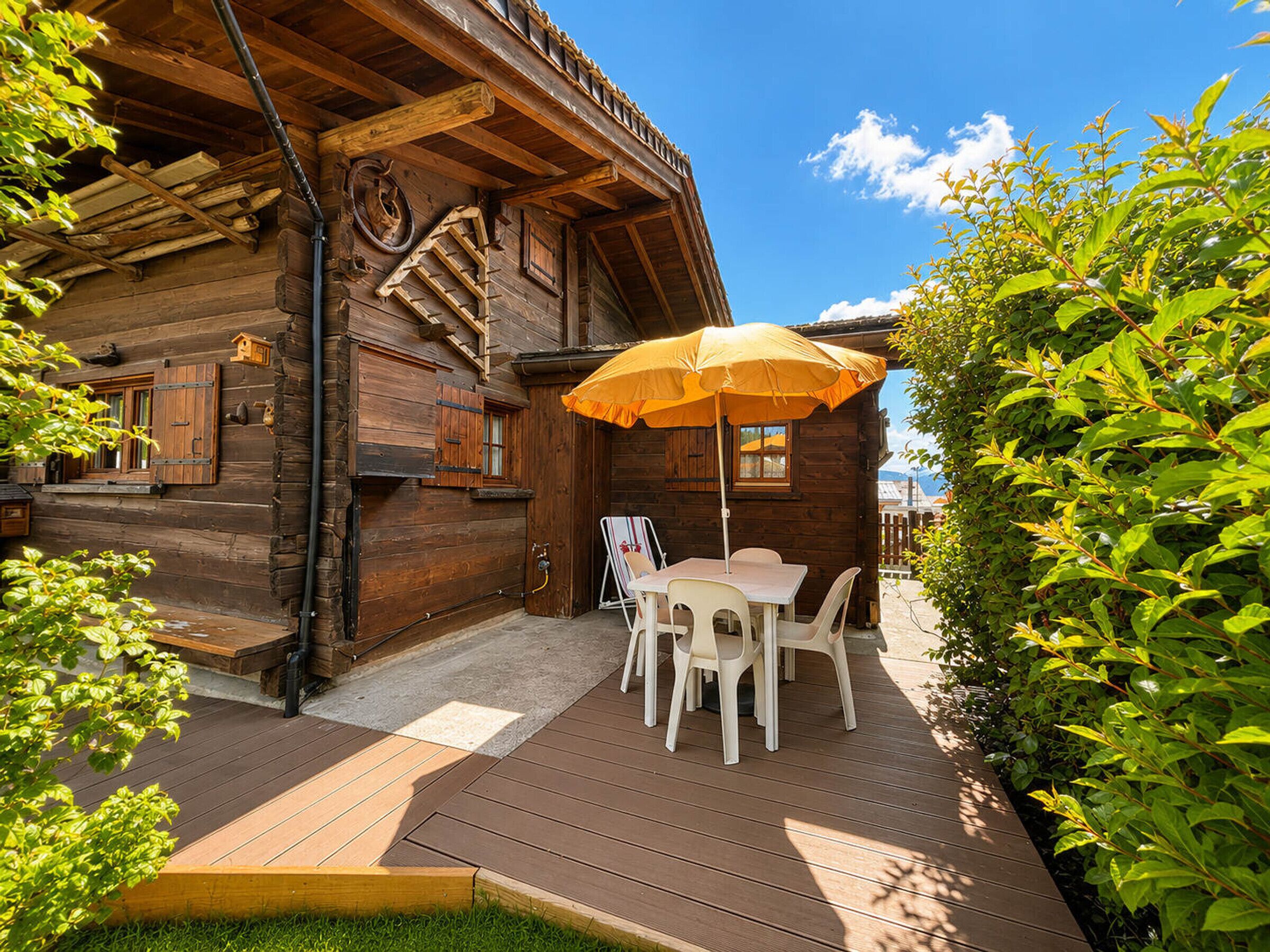 A wooden cabin with a deck, outdoor seating, and a large umbrella.