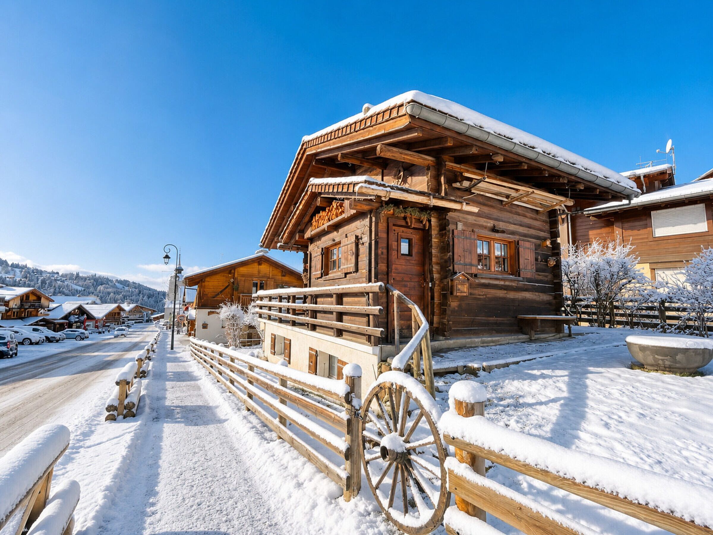 A wooden chalet with a snow-covered roof, a wooden fence, and a snow-covered ground.