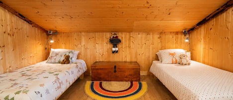 A cozy room with two beds, a wooden ceiling, and a central nightstand.