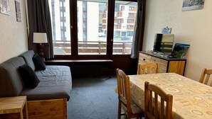 A compact room with a sofa, a small wooden table, a dining table with chairs, a TV, and a window with a view of buildings. - Tignes: Apartment 6 pers, 41 sqm, Slope View (Tignes)