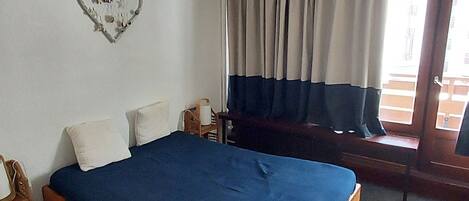 A bedroom with a wooden bed, a white wall, a heart-shaped decoration, and a window with curtains.