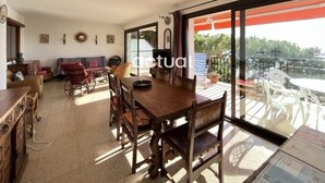 A spacious living area with a wooden dining table, wicker chairs, and a sofa. A large sliding glass door leads to an outdoor patio with white chairs and a table. - Seafront apartment with terrace and parking in Platja d'Aro (Platja d'Aro)