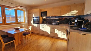 Eine moderne Küche mit Holzschränken, einem Esstisch mit Stühlen und einem großen Fenster.