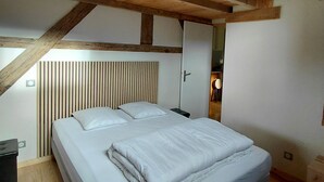 A bedroom with a wooden ceiling, a bed with white bedding, a bedside table, and a wall-mounted light.