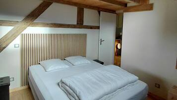 Une chambre avec un plafond en bois, un lit avec une literie blanche, une table de chevet et une lampe fixée au mur.