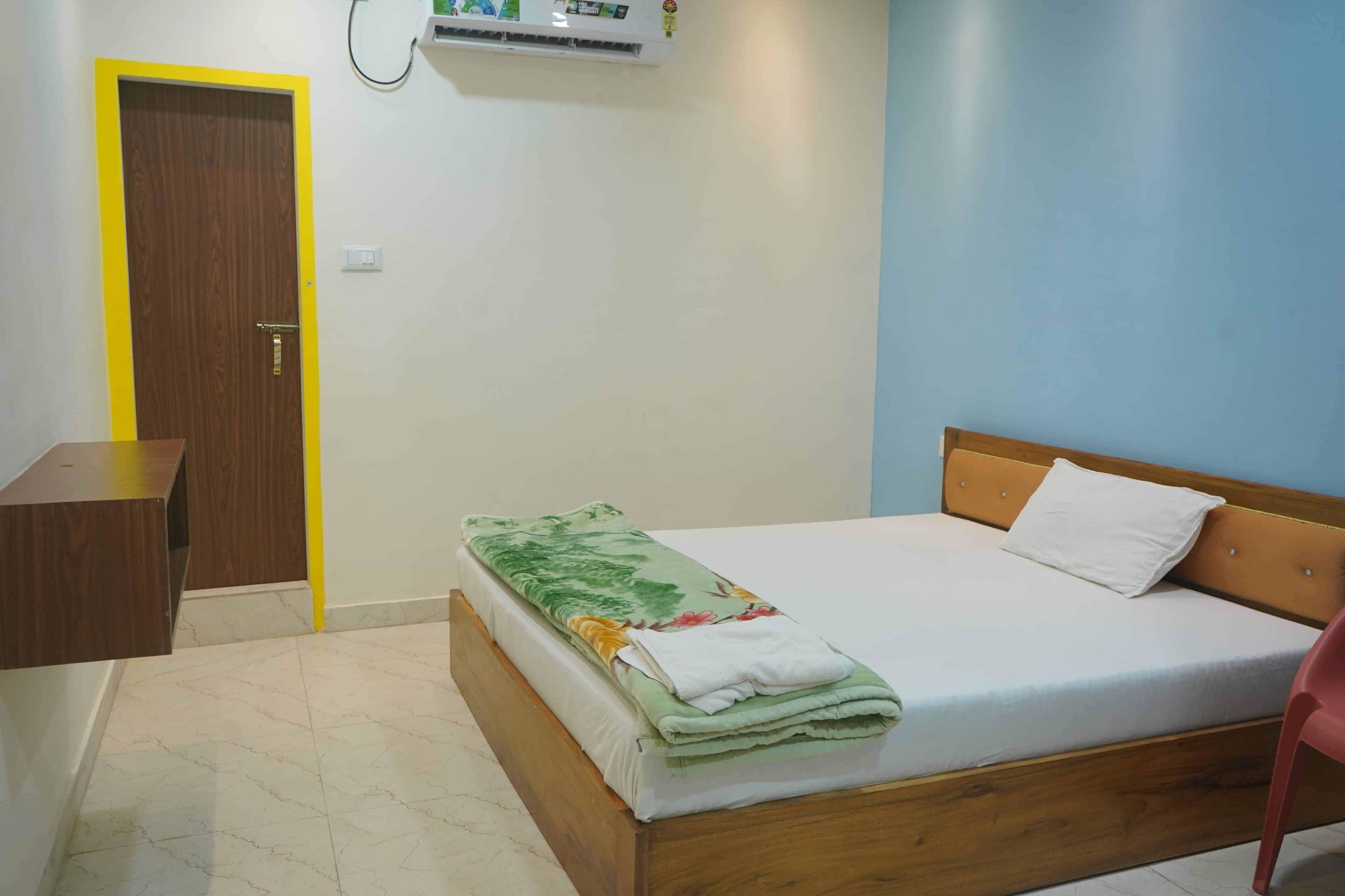 A bedroom with a bed, a wooden nightstand, a desk, and a door.