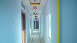 A long, narrow hallway with light blue walls and a yellow stripe. There are doors on both sides and a series of hanging decorative lights along the ceiling. - Hotel Aaradhya (Guwahati)
