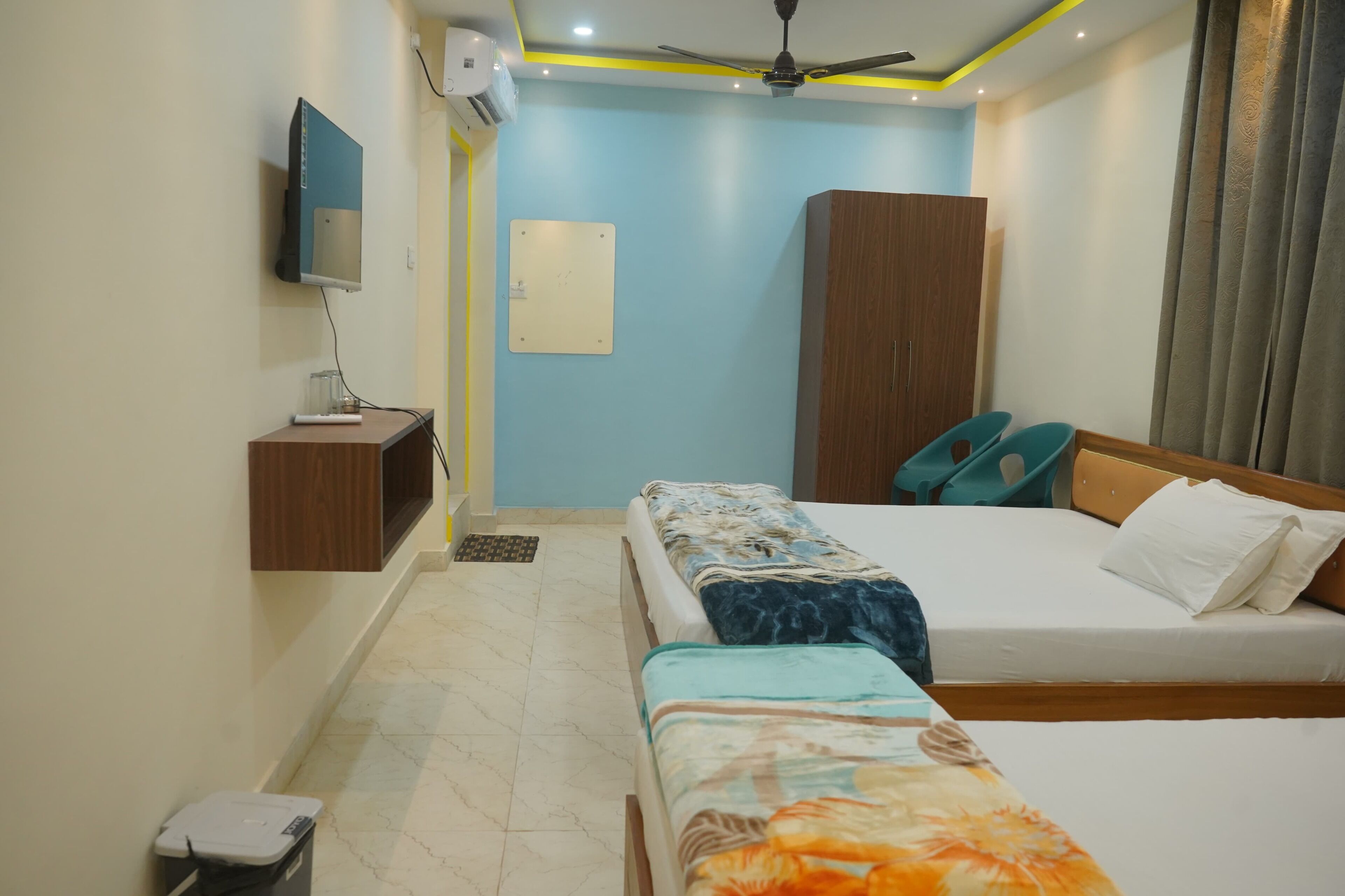 A hotel room with two beds, a TV mounted on the wall, a wardrobe, and a ceiling fan.