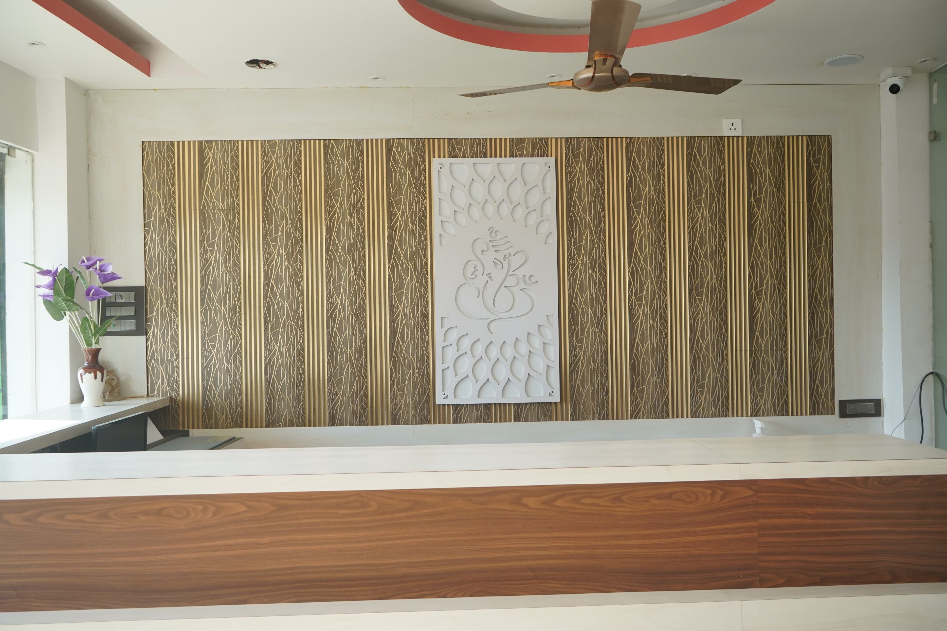 A reception area with a patterned wall, a decorative panel, a ceiling fan, and a potted plant.