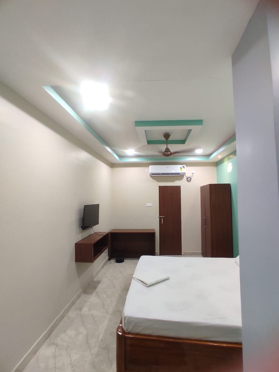 A bedroom with a bed, a TV, a wardrobe, and a ceiling fan.