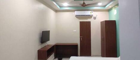 A bedroom with a bed, a TV, a wardrobe, and a ceiling fan.