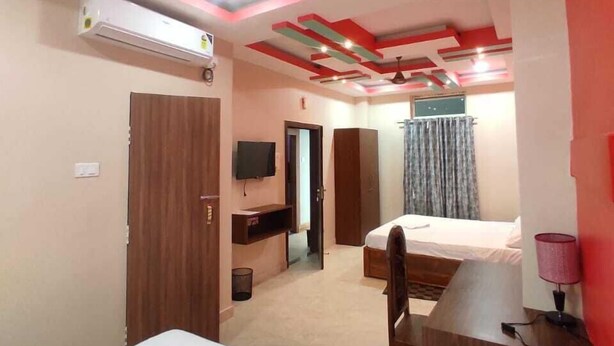 A hotel room with two beds, a desk, a TV, and a ceiling fan. - Hotel Aaradhya (Guwahati)